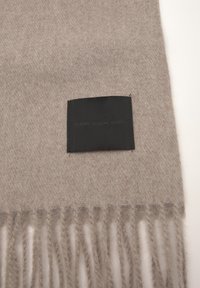 Svetlo rjav woven šal z resastimi konci in črno pravokotno nalepko z napisom "KLASIKA. SODOBNO. VAŠE."