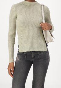 Pull à manches longues côtelé de couleur vert clair, doté d'un col montant et d'une finition texturée. Associé à un jean gris foncé et un sac à main clair.