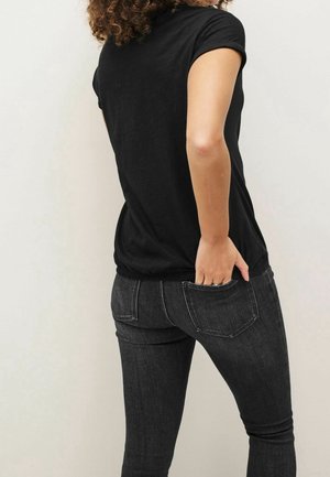 Black short-sleeve t-shirt with a rounded hem, worn with dark grey slim-fit jeans. The fabric appears soft with a slight sheen.