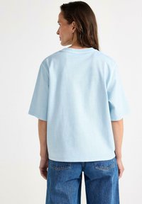 Lyseblå oversized bomulds-t-shirt med korte ærmer, rund halsudskæring og en glat tekstur; kombineret med løse denimbukser.