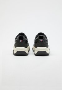 Zwarte sportieve schoenen met een glad leren bovenwerk, witte middenzool en gestructureerde rubberen buitenzool, met een kleine driekleurige accent op de hiel.