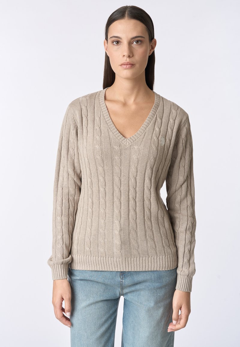 Maglione beige a maglia con scollo a V, polsini e orlo a coste. Presenta un motivo testurizzato e una vestibilità morbida. Abbinato a jeans azzurri chiari.