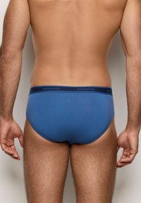 Slip in cotone blu da uomo con design a vita bassa e un elastico scuro con il nome del marchio "yamamay." Texture liscia, dettagli minimi.
