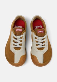 Brązowe i kremowe sneakersy z białymi sznurowadłami i czerwonymi wkładkami, z logo "Camper" na języku, przedstawione z góry.