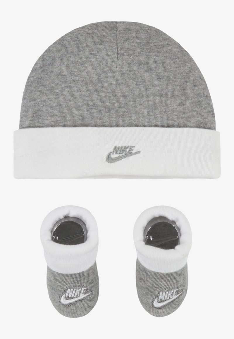 Beanie grigio a maglia con risvolto bianco; presenta il logo Nike. Due scarpine abbinate con texture morbida e logo; schema di colori grigio e bianco.