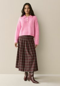 Rausvas pūkuotas megztinis su apykakle ir sagų užsegimu, derinamas su burgundiškos ir žalios spalvų languota maksi sijonu bei blizgiais burgundiškais aukštakulniais batais.