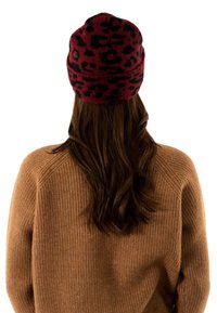 Gorro de leopardo rojo y negro, hecho de material de punto suave. Lo lleva una modelo con el cabello largo y oscuro, combinado con un suéter beige.