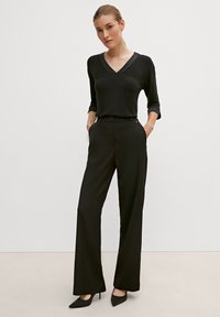 Czarny top z dekoltem w serek i rękawami 3/4, zestawiony z czarnymi spodniami o wysokim stanie. Dopasowany krój, gładki materiał i czarne czółenka na szpilce.