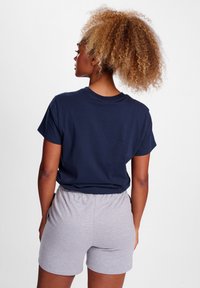 Mörkblå bomullströja med korta ärmar, tillsammans med grå shorts med elastiskt midjeband. Modellen ses från ryggen.