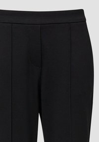Pantalon noir sur mesure avec une ceinture plate et des coutures centrales devant, montré de la taille jusqu'au milieu de la cuisse sur un fond uni.