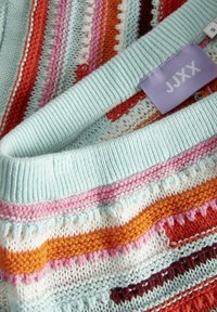 Suéter de punto con rayas horizontales multicolores: azul claro, naranja, rosa y rojo. Presenta un cuello acanalado y una etiqueta de tela etiquetada como "JJXX."