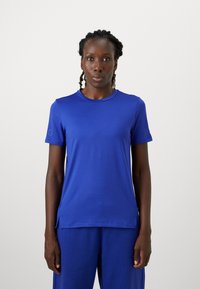 Zils sportiska t-krekls ar īsām piedurknēm, noapaļotu kakla izgriezumu un sānu šķelumiem. Izgatavots no gludas, vieglas auduma ar smalku zīmola izvietojumu uz piedurknes.