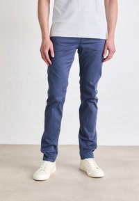 Pantalones de algodón azules con un corte slim, que cuentan con bolsillos laterales y una textura suave, combinados con zapatillas blancas con cordones.
