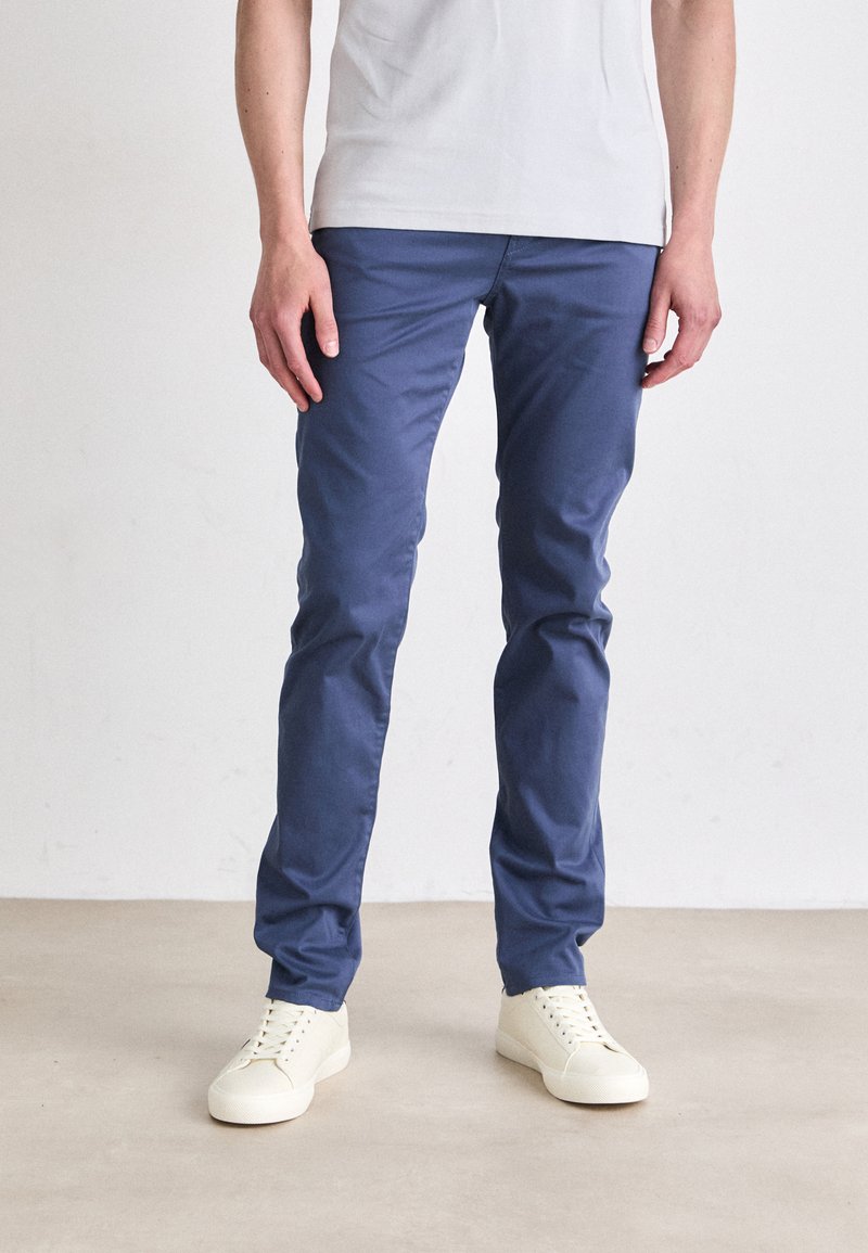 Pantalones de algodón azules con un corte slim, que cuentan con bolsillos laterales y una textura suave, combinados con zapatillas blancas con cordones.