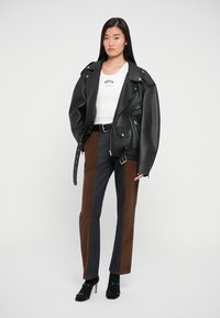Schwarze Leder-Motorradjacke mit übergroßer Passform, kombiniert mit farblich abgesetzten Cordhosen in Braun und Grau. Schwarze High-Heels.