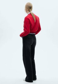Red sweatshirt with a relaxed fit, paired with high-waisted black jeans. The fabric appears soft, and the jeans feature a classic five-pocket design.