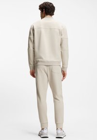 Beige sweatshirt met een ronde hals, verzakte schouders en geribbelde manchetten, gecombineerd met bijpassende taps toelopende broeken en witte sportschoenen.