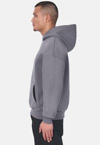 Grijze hoodie van zachte stof, met een kangoeroezak, een trekkoordcapuchon en ribgebreide manchetten. Gladde textuur met minimale branding.