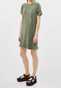 Olivgrön bomullst-shirtklänning med korta ärmar och sidofickor. Matchad med svarta plattformssandaler med justerbara remmar.