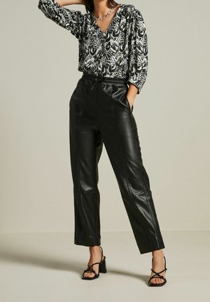 Pantalons en cuir noir avec taille à cordon, associés à un blouse à col en V noir et blanc à motif avec des manches volumineuses.