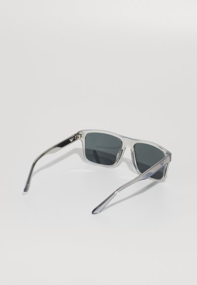 Ochelari de soare cu ramă transparentă, lentile gri, formă rectangulară și accente metalice pe brațe. Prezintă logo-ul brandului pe templul stâng.