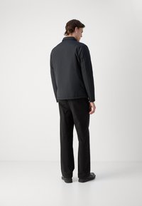 Schwarze gepolsterte Jacke mit Kragen, Rückennähten und langen Ärmeln. Kombiniert mit schwarzen Hosen und einer glatten Sohle. Minimalistisches Design.