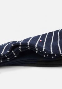 Marineblaue Socken mit weißen senkrechten Streifen, aus einem weichen Material gefertigt. Besitzen ein kleines rotes Akzentlogo. In einer ordentlichen Anordnung gestapelt.