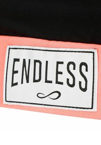 Parche rectangular blanco con borde negro y texto "ENDLESS" sobre un símbolo de infinito, cosido en un fondo de tela negra y coral.