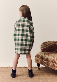 Grünes und weißes karierter Hemdkleid mit langen Ärmeln, einem Kragen und lockerem Sitz; kombiniert mit schwarzen Stiefeletten und pinkfarbenen Socken.