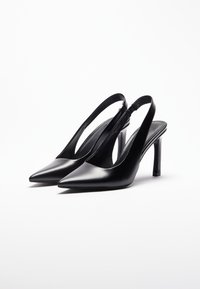 Black patent leather slingback heels with a pointed toe, open side cutouts, and a slender high heel. Smooth texture with minimal detailing.