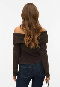 Pull marron à manches longues avec épaules découvertes, fabriqué en matière douce, associé à un jean denim bleu foncé avec poches arrière.