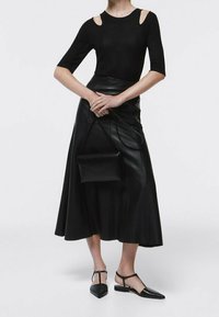 Top aderente nero con dettagli a spalla scoperta, abbinato a una gonna midi fluida in pelle nera e scarpe nere basse. Piccola borsa a tracolla nera.