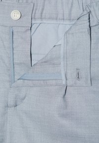 Pantaloni azzurri chiari realizzati in un tessuto testurizzato, con chiusura a bottone e tasca con zip. Il girovita è elasticizzato per maggiore comfort.