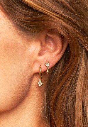 Gouden oorringen met een bloemdesign, heldere kristallen, een kleine hartaccent en een hangende druppel charm.