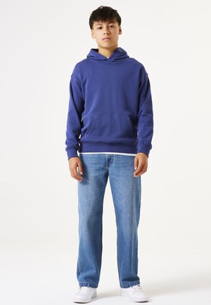 Sudadera de algodón azul con un bolsillo frontal y capucha con cordón, combinada con unos pantalones vaqueros azul claro y zapatillas blancas. Diseño simple, corte relajado.