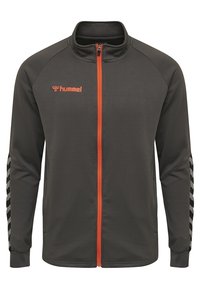 Mörkgrå zip-up jacka i texturerat material, med orange dragkedja och logotyp, samt svarta och vita chevron-accenter på ärmarna.