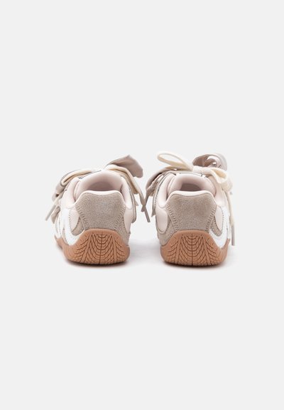 Paire de baskets beige et blanche avec semelles en caoutchouc couleur noisette, vue de dos, posée sur un fond blanc uni.