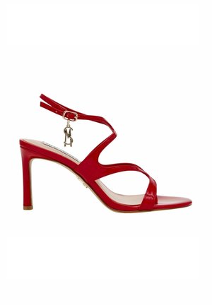 Sandalo con tacco alto in pelle verniciata rossa, dal design con strappi, fibbia alla caviglia e piccolo charm decorativo. Punta aperta e superficie liscia.