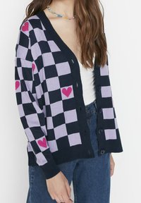 Granatowy i lawendowy kardigan w kratę z różowymi akcentami w kształcie serca, z dekoltem w serek, zapięciem na guziki i ściągaczami przy mankietach. Miękki materiał dzianinowy.