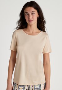 T-shirt beige a maniche corte con scollatura rotonda, texture liscia e vestibilità comoda, abbinato a pantaloni con fantasie dai colori vivaci.