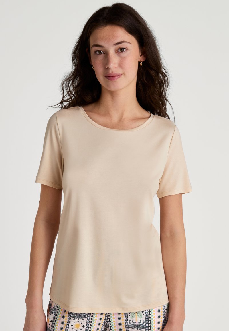 T-shirt beige a maniche corte con scollatura rotonda, texture liscia e vestibilità comoda, abbinato a pantaloni con fantasie dai colori vivaci.
