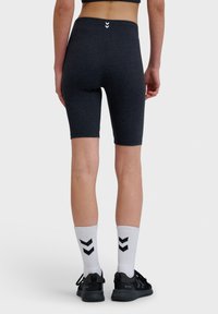 Mörkgrå cykelshorts gjorda av stretchtyg, med ett högt midjeband och en liten vit logotyp på baksidan. Kombinerat med svarta skor och vita strumpor.