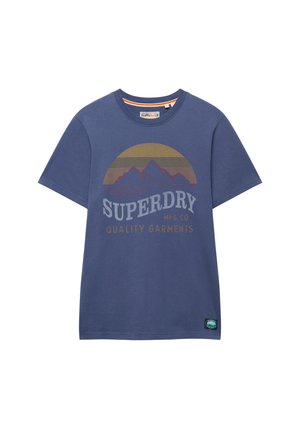 Camiseta azul de manga corta con gráfico de montaña, fondo de atardecer y texto "SUPERDRY MFG. CO QUALITY GARMENTS" en la parte delantera.