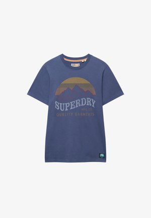 Camiseta azul de manga corta con gráfico de montaña, fondo de atardecer y texto "SUPERDRY MFG. CO QUALITY GARMENTS" en la parte delantera.