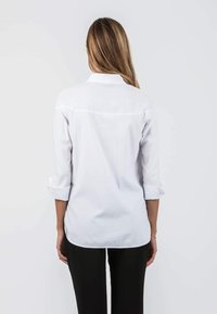 White long-sleeve shirt with rolled cuffs, featuring a curved hem and a smooth texture. Back view highlights simple design and fit.