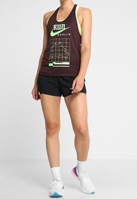 Maroon urheilullinen tankkitoppi, jossa on "RUN BERLIN" -graafinen printti ja karttasuunnittelu; yhdistetty mustiin shortseihin ja valkoisiin kenkiin, joissa on värikkäitä yksityiskohtia.