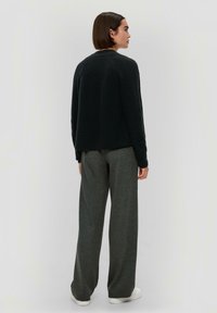 Schwarzer gerippter Strickpullover mit rundem Ausschnitt, kombiniert mit grauen weiten Hosen und weißen Sneakers. Das Outfit zeichnet sich durch eine lockere Passform aus.
