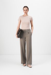 Light pink fitted t-shirt, high-waisted beige trousers with side pockets, and flat nude shoes. A dark clutch bag is held in the left hand.