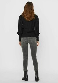 Black long-sleeve top with puffed shoulders paired with gray skinny jeans. Model wears black ankle boots with a textured finish.