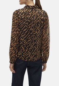 Blouse noire transparente avec imprimé animal brun, manches bouffantes et col. Bas resserré et empiècement arrière détaillé. Associée à un denim foncé.